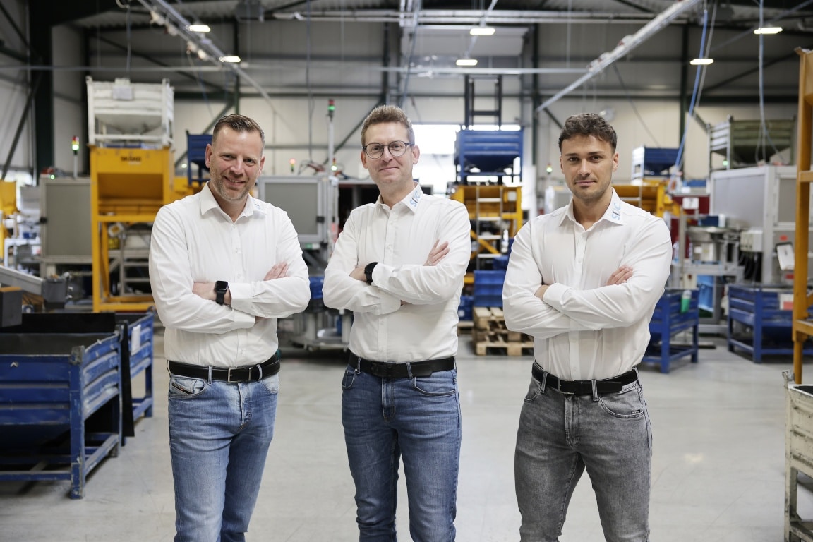 Drei Männer in Produktionshalle mit verschränkten Armen